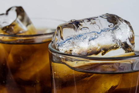 Cold drink with ice in a glass on a white table. A way to cool down on hot days. White background.