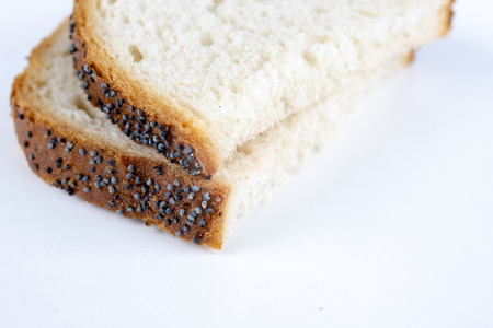 A slice of bread on a white kitchen table. Bread with poppy seeds cut into pieces. White background.