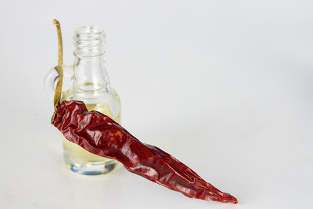 Dried peppers and a vial of oil on a white kitchen table. Spices helpful in preparing dishes. White background.の写真素材