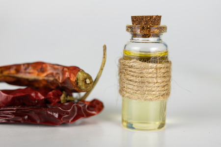 Dried peppers and a vial of oil on a white kitchen table. Spices helpful in preparing dishes. White background.の写真素材