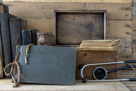 Stethoscope and a case on an old desk. Medical magazines and medical accessories on a wooden table. Dark background.の写真素材