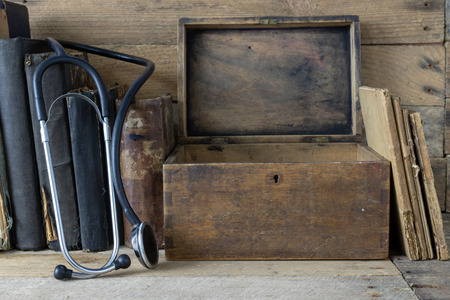 Stethoscope and a case on an old desk. Medical magazines and medical accessories on a wooden table. Dark background.の写真素材