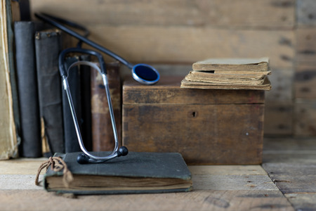 Stethoscope and a case on an old desk. Medical magazines and medical accessories on a wooden table. Dark background.の写真素材