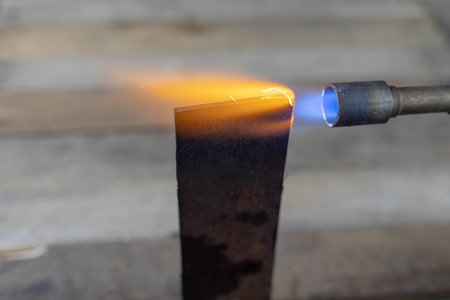 Metal heating with a gas burner in a home workshop. Tempering steel with flames. Dark background.