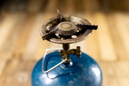 An old gas burner for preparing dishes. Tourist accessories on an old wooden table. Dark background.
