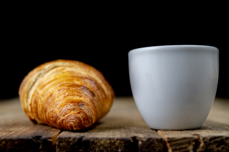 Tasty well-baked croissant on a wooden kitchen table. Light bread prepared for breakfast. Dark background.の写真素材