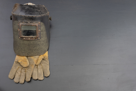 Welder's mask and gloves on a black workshop table. Protective clothing for workers in metalware. Dark background.の写真素材