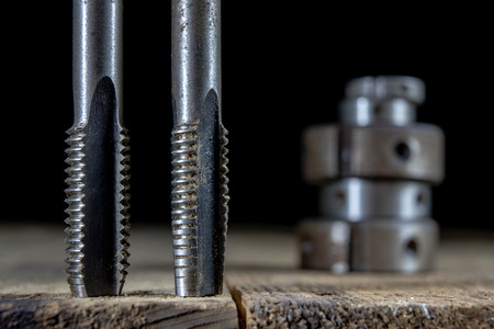 Metalwork tools on the workshop table. Threading dies and taps in an old dusty workshop. Black background.の写真素材