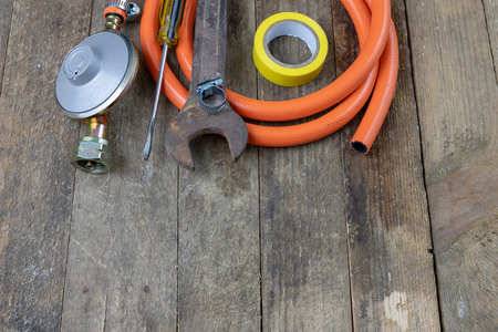 Regulator for propane-butane gas cylinder and accessories on a wooden workshop table. Gas accessories in the workshop. Dark background.の写真素材