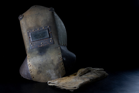 An old mask a protective suit for a welder. Occupational health and safety clothing for production workers on a workshop table. Black background.の写真素材
