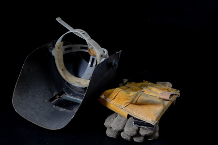 An old mask a protective suit for a welder. Occupational health and safety clothing for production workers on a workshop table. Black background.の写真素材