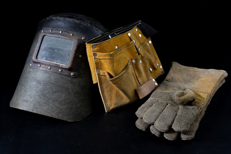 An old mask a protective suit for a welder. Occupational health and safety clothing for production workers on a workshop table. Black background.の写真素材