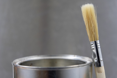 A paint brush and a can of paint on a workshop table. Painting accessories for construction workers. Light background.の写真素材