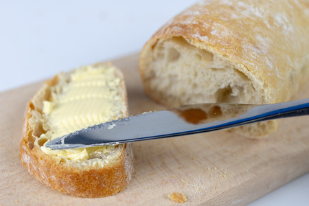 Fresh bread on a wooden kitchen board. A slice of bread smeared with butter. light background.