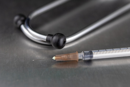 Syringes for insulin delivery and a stethoscope on a metal table. Medical accessories at the medical point. Dark background.の写真素材