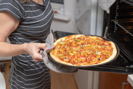 Baking a delicious pizza in a home kitchen. Slicing and stacking the baked pizza on the kitchen table. Light background.の写真素材