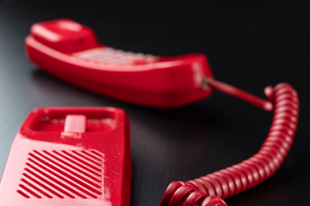 Old analog telephone. Red phone on a wooden dark table. Black background.の写真素材