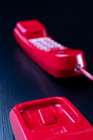 Old analog telephone. Red phone on a wooden dark table. Black background.の写真素材