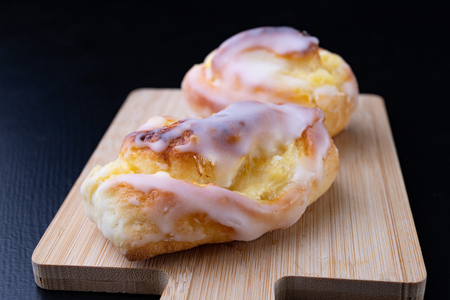 Sweet roll with icing on a small board. Tasty dessert on the kitchen table. Dark background.の写真素材