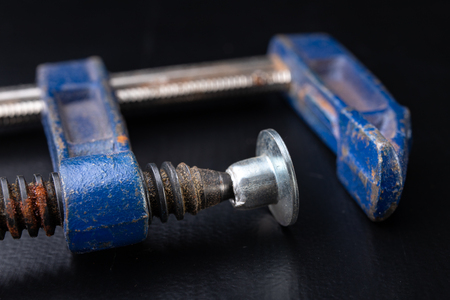 An old carpentry clamp on a workshop table. Accessories for carpenters. Dark background.の写真素材