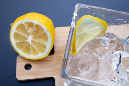 Cold drink in a glass on the kitchen table. Lemon and ice with water the best way to cool off on a summer day. Dark background.の写真素材