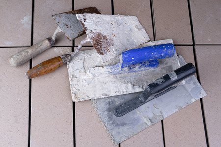 Tiles cut to size and trowels for applying mortar. Masonry accessories on a workshop table. Dark background.の写真素材