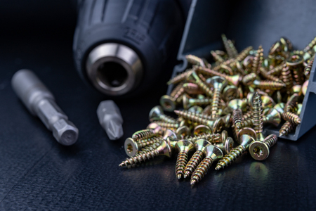 Screws in a box and a screwdriver on a workshop table. Accessories for DIY. Dark background.