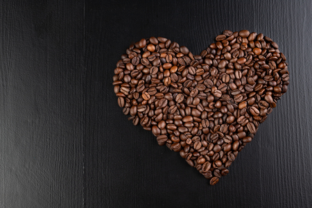 Roasted coffee beans arranged in the shape of a heart on the table. Tasty fragrant coffee in the kitchen. Dark background.の写真素材