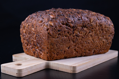 Tasting bread with seeds on a wooden board. Fresh dark bread on the kitchen table. Dark background.