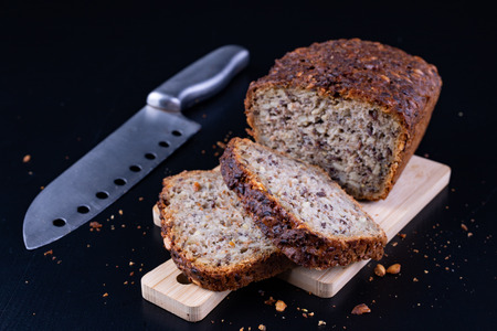 Tasting bread with seeds on a wooden board. Fresh dark bread on the kitchen table. Dark background.の写真素材