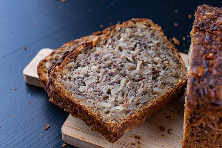Tasting bread with seeds on a wooden board. Fresh dark bread on the kitchen table. Dark background.