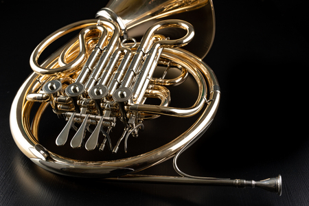French horn on a wooden table. Beautiful polished musical instrument. Dark background.の写真素材