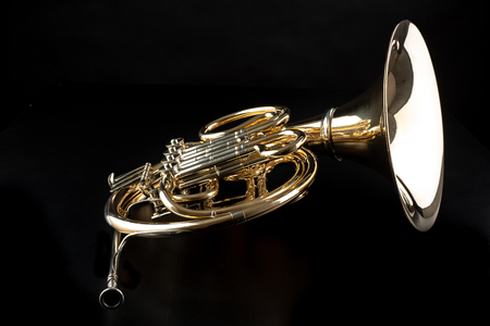 French horn on a wooden table. Beautiful polished musical instrument. Dark background.の写真素材