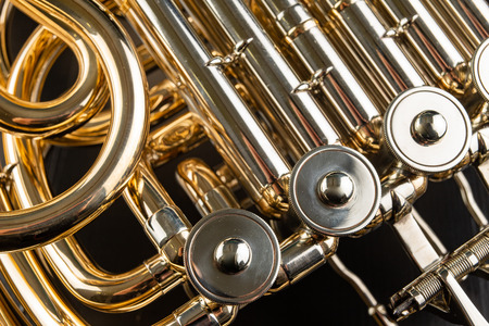 French horn on a wooden table. Beautiful polished musical instrument. Dark background.