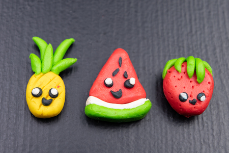 Plasticine figurines on a dark wooden table. Imitation of pineapple, watermelon and strawberry fruit. Dark background.の写真素材