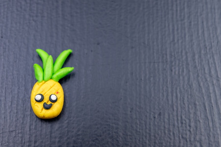 Plasticine figurines on a dark wooden table. Imitation of pineapple fruit. Dark background.