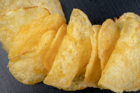 Tasty crisps on the kitchen table. Salty snacks as an addition to beer. Dark background.