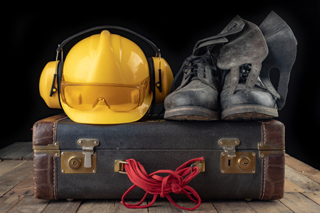Helmet shoes and gloves on a travel suitcase. Working clothes prepared for traveling on a work table. Dark background.の写真素材