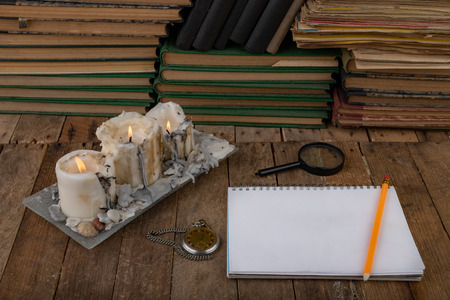 Burned candle and a notebook on an old wooden table. Workplace of the writer. Dark background.の写真素材
