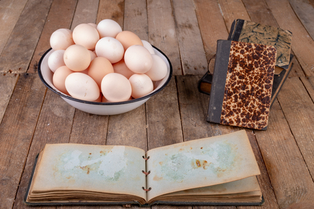 Eggs from hens and an old notebook on a wooden kitchen table. Fresh rye sprouts in a porcelain bowl. Dark background.の写真素材