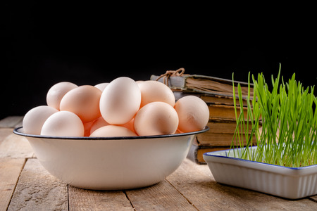 Eggs from hens on a wooden kitchen table. Fresh rye sprouts in a porcelain bowl. Dark background.