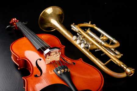 A new shining violin and an old trumpet on a dark table. Musical instruments, stringed and wind. Black background.の写真素材