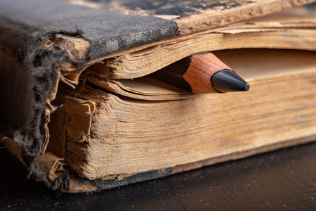 Colorful pencils on an old book. Books in old covers and coloring pencils. Dark background.の写真素材