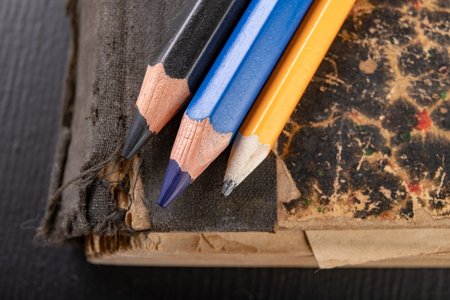 Colorful pencils on an old book. Books in old covers and coloring pencils. Dark background.の写真素材