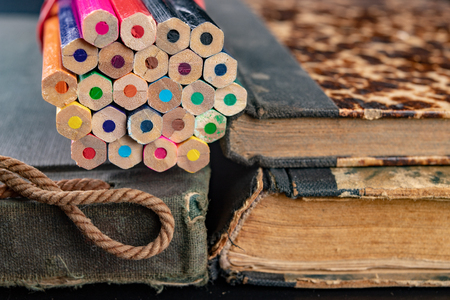 Colorful pencils on an old book. Books in old covers and coloring pencils. Dark background.の写真素材