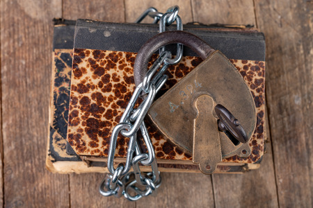 Old books bound by a new shiny chain with an old padlock. Forbidden old works artists on a wooden table. Dark background.の写真素材