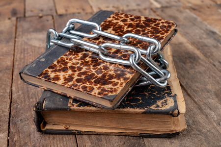 Old books related to a new shiny chain. Forbidden old works artists on a wooden table. Dark...