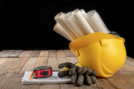 Construction helmet and roll of parchment with design. Construction engineer accessories on a wooden...