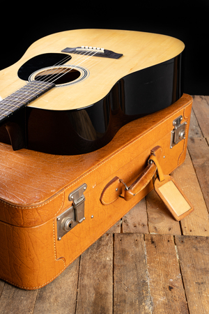 Classical guitar and suitcase on a dark wooden table. Stringed musical instrument on the go. Black background.の写真素材