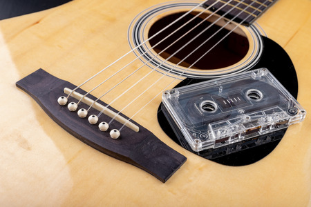Acoustic guitar and cassette tape. Musical instrument and old music carrier. Dark background.